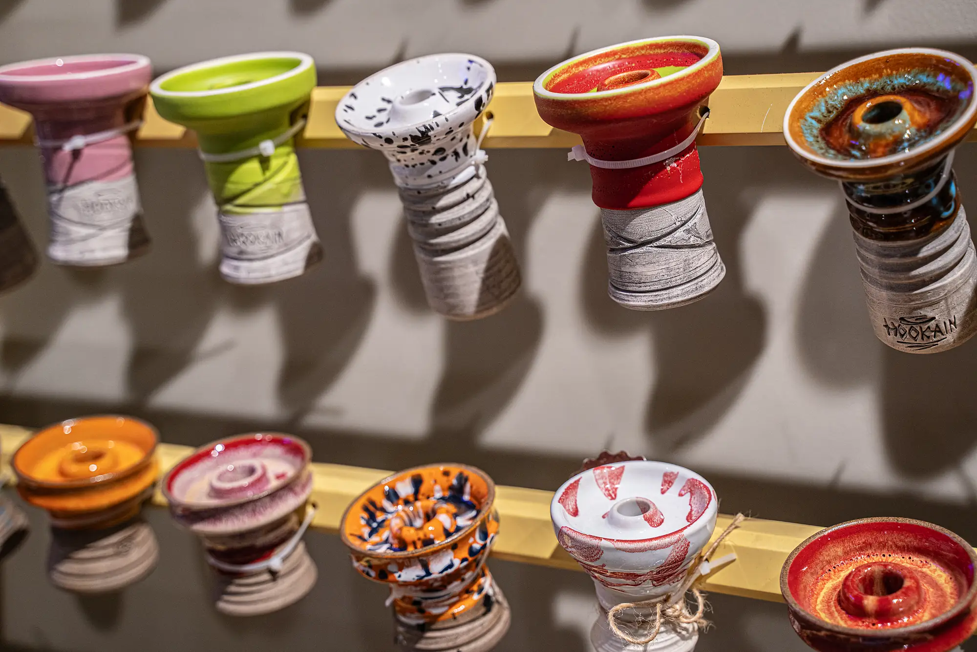 Bunte Shisha-Köpfe in Pink, Grün, Rot und Orange an der Wandhalterung bei SmokeFactory Köln