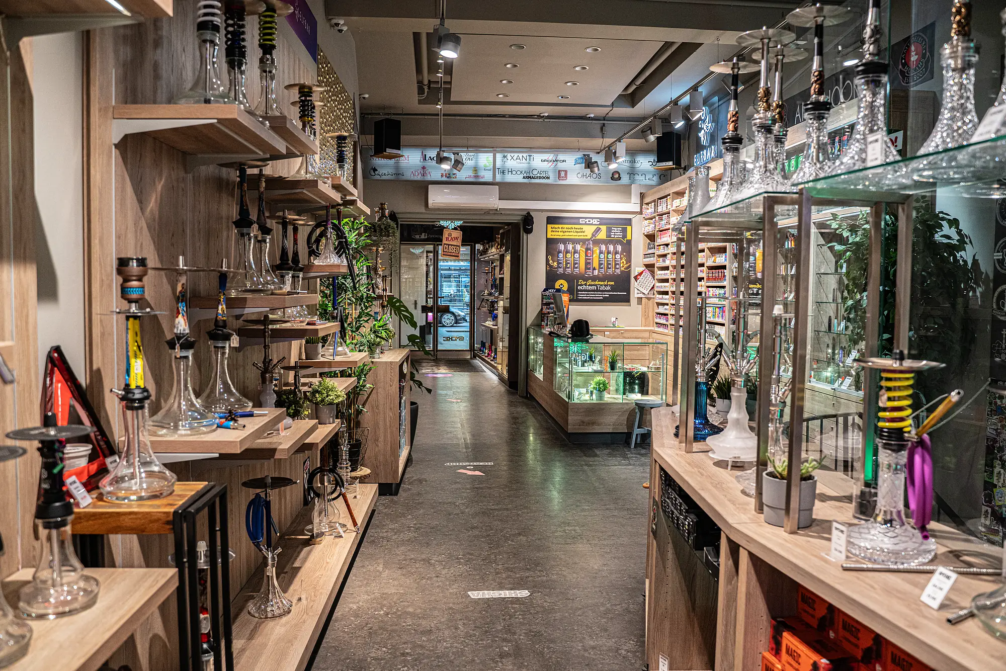 Blick in den SmokeFactory-Laden am Kölner Neumarkt — Shisha-Regale, Kristall-Shishas in Glasvitrinen und Tabakwand