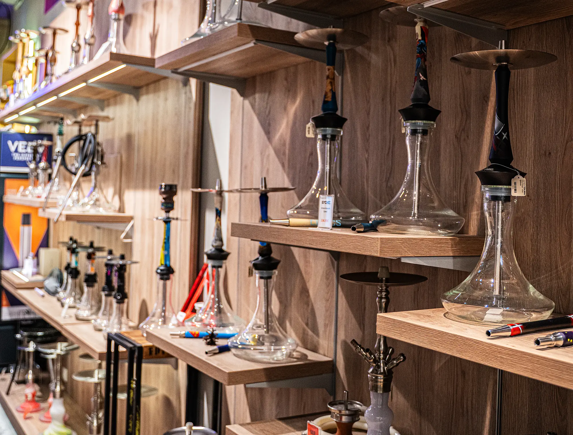 Holzregalwand voller Glas-Shishas in vielen Formen bei SmokeFactory Köln am Neumarkt