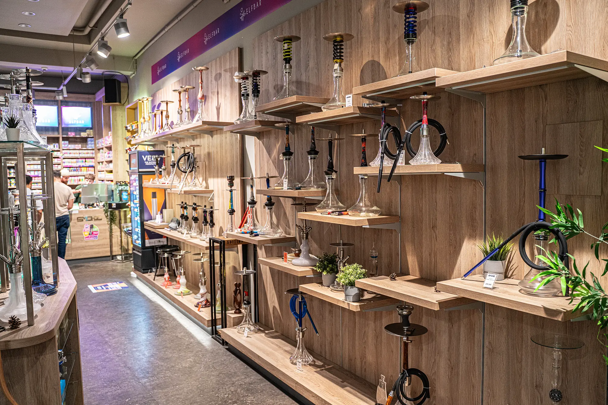 Lange Holzregalwand voller Shishas und Zubehör im SmokeFactory-Laden am Neumarkt